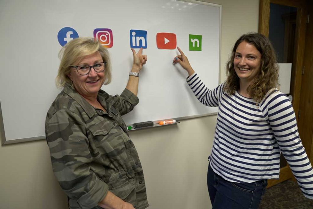 Two Paragon employees pointing to different social media channels on a whiteboard