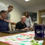 Close up of the Paragon Marketing team at a desk, with the focus on a coffee mug. Consider Paragon's marketing solutions for your business.