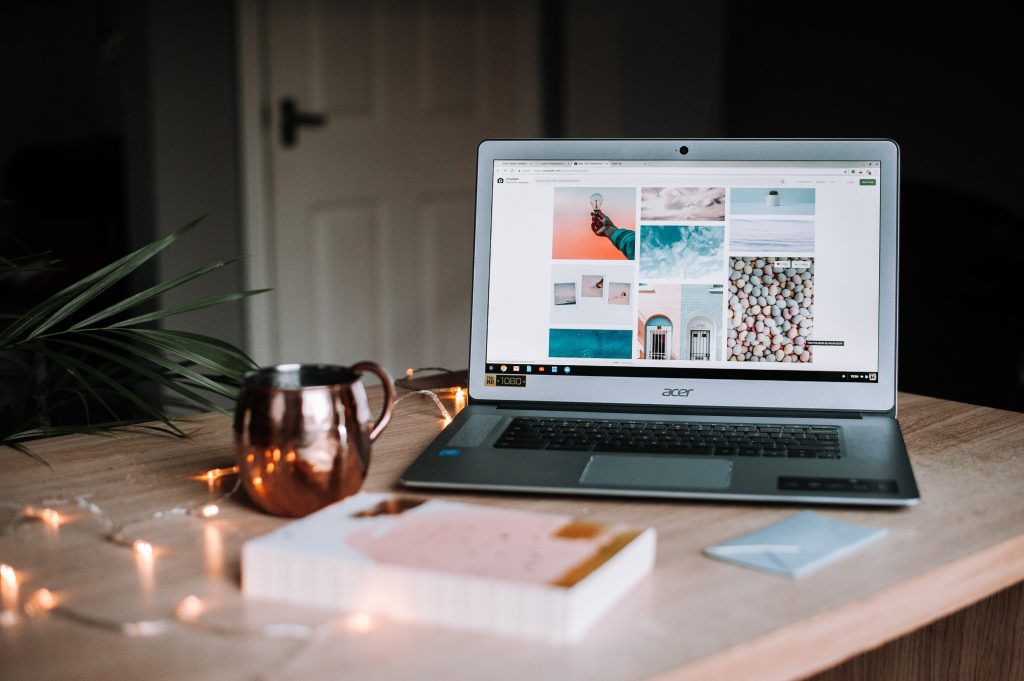 A laptop, mug, and book on a desk. The workplace is set up for a person to use holiday marketing tips for their business this season.